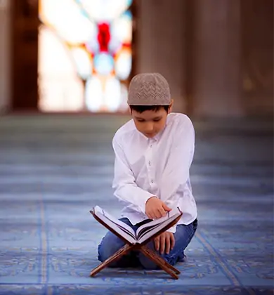 The child is practicing the Tajweed course while reading the Holy Quran and offering prayer in the mosque.