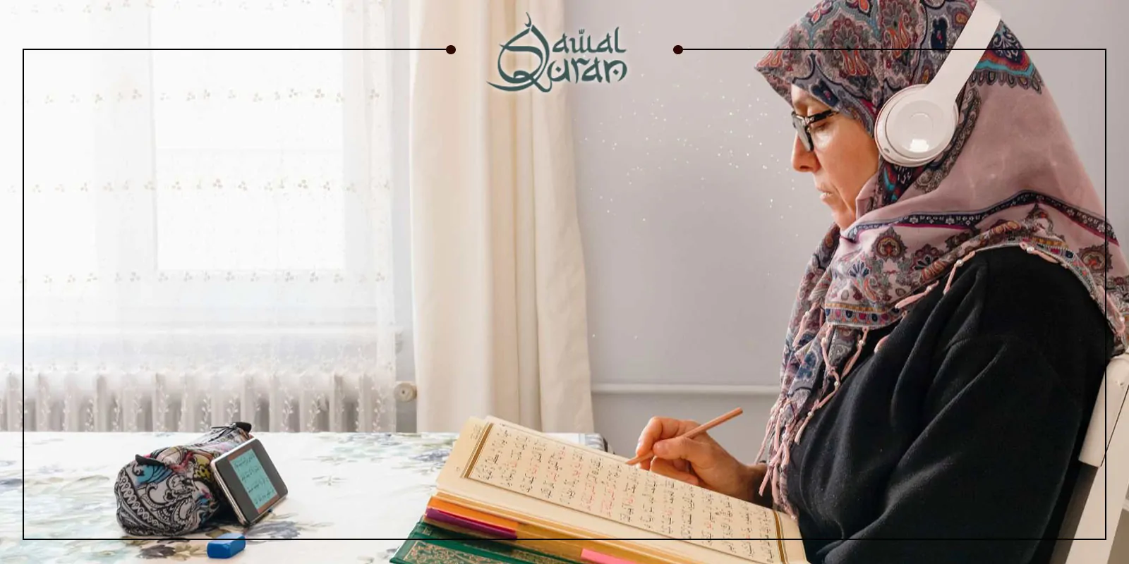 A woman in a hijab wears headphones and studies the Quran online at a table, holding a pencil and looking at an open book, with a tablet and pencil case nearby.